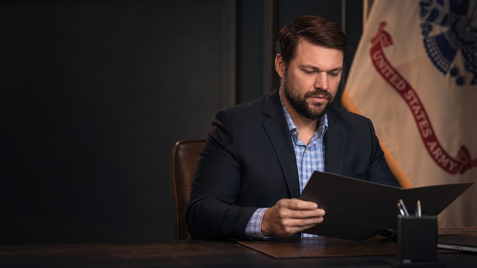 Blake Kamoroff reviewing a military case file with a U.S. Army flag in the background